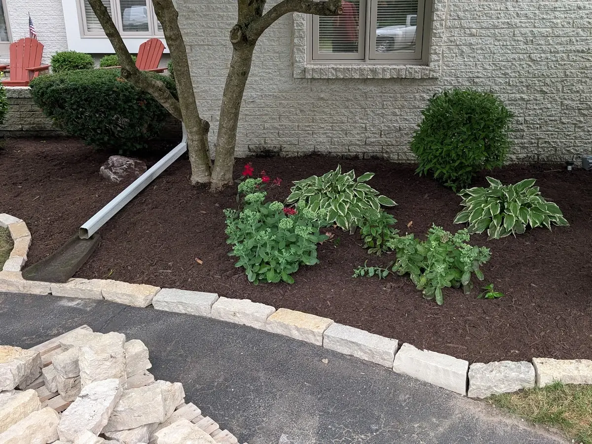 Mulched flower bed with a stone border and a pile of stone in the foreground