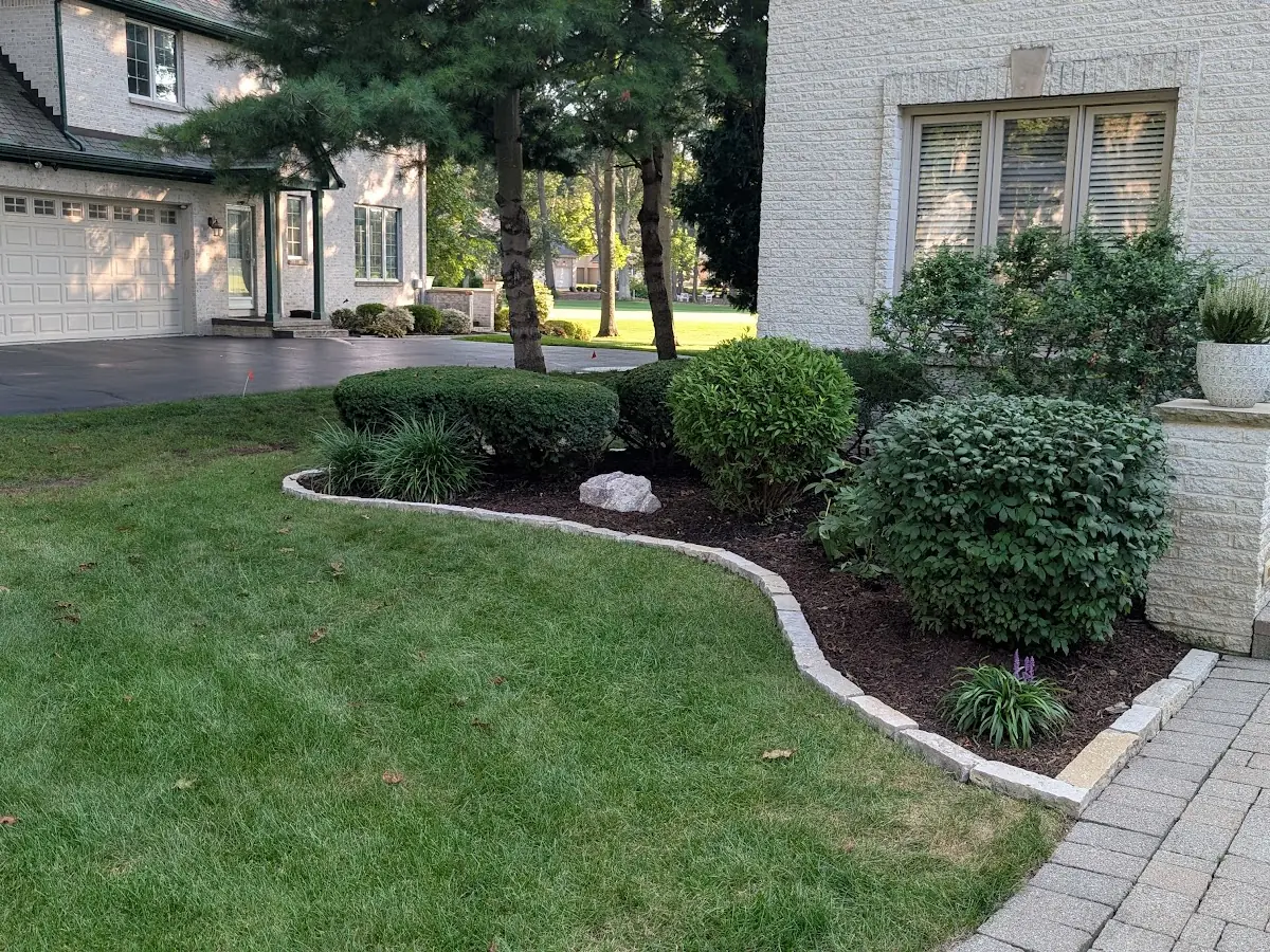 Stone-edged mulch bed with shrubs next to front steps and a paver walkway