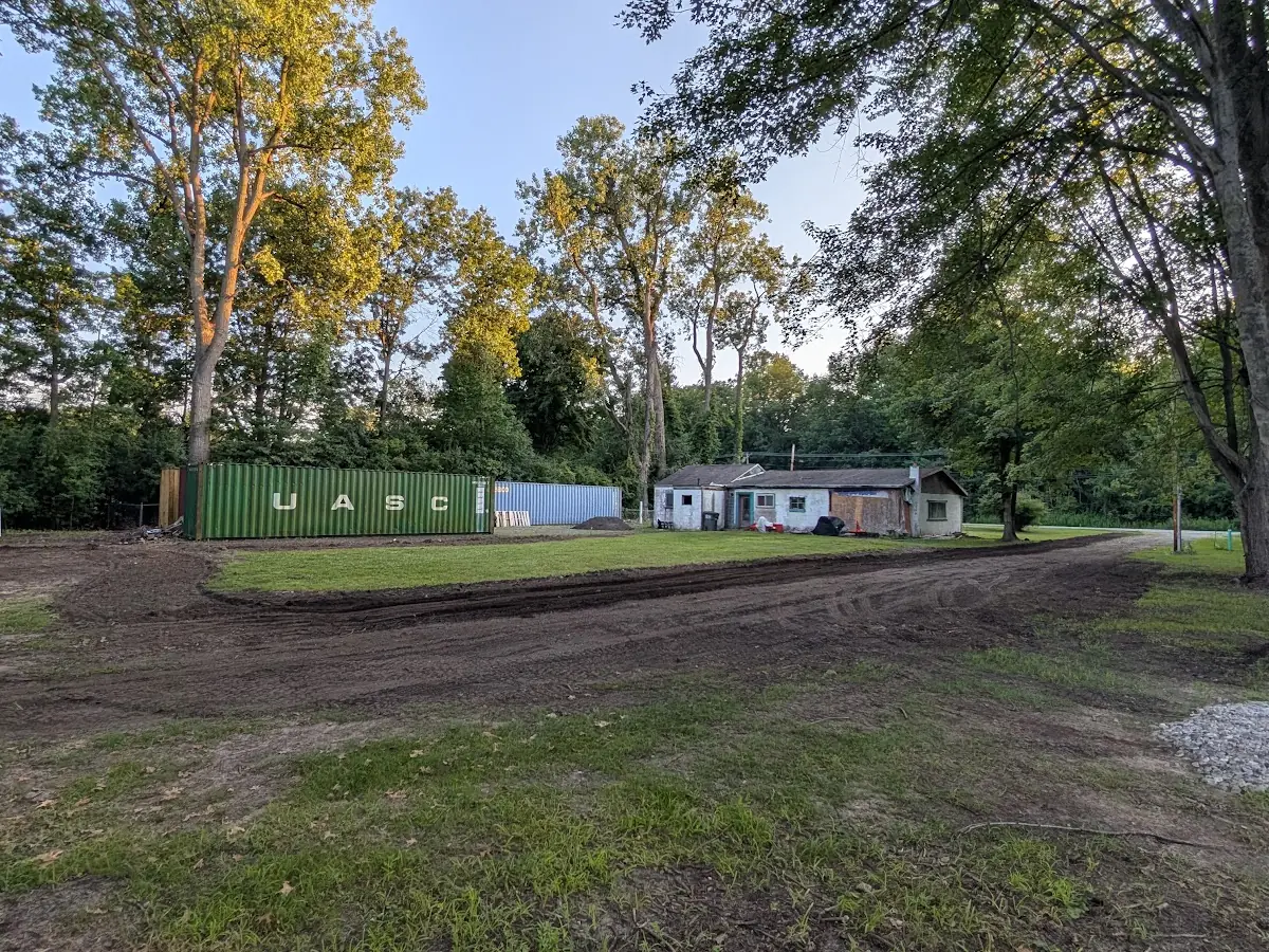 Cleared and graded open area with shipping containers and a small building in the background