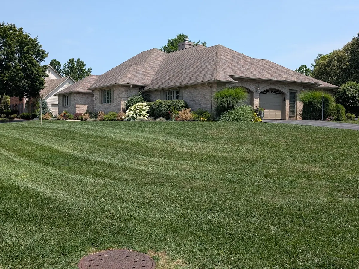 Mowed lawn with straight stripes in front of a brick house with landscaping beds
