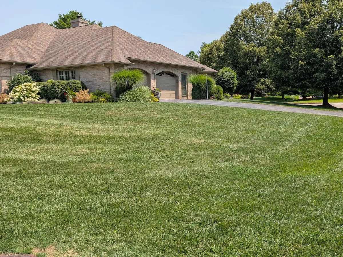 Mowed lawn curving along a driveway beside a brick house