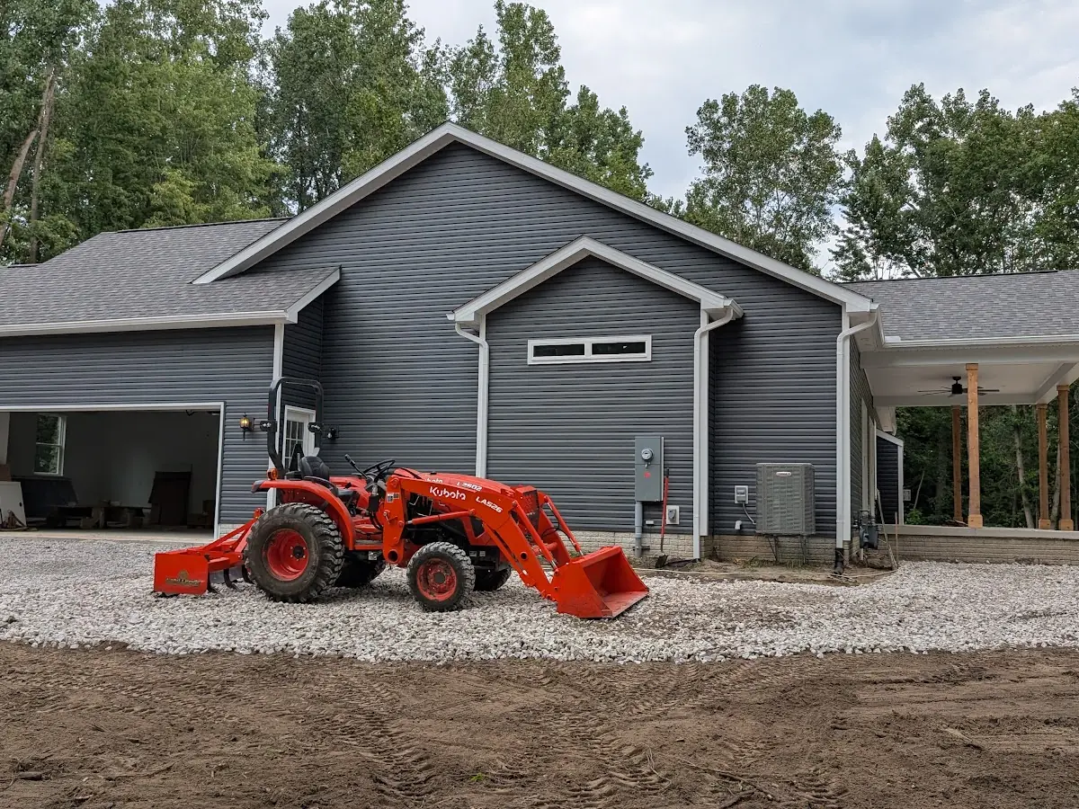 Orange compact tractor on a new crushed-stone driveway beside a gray garage