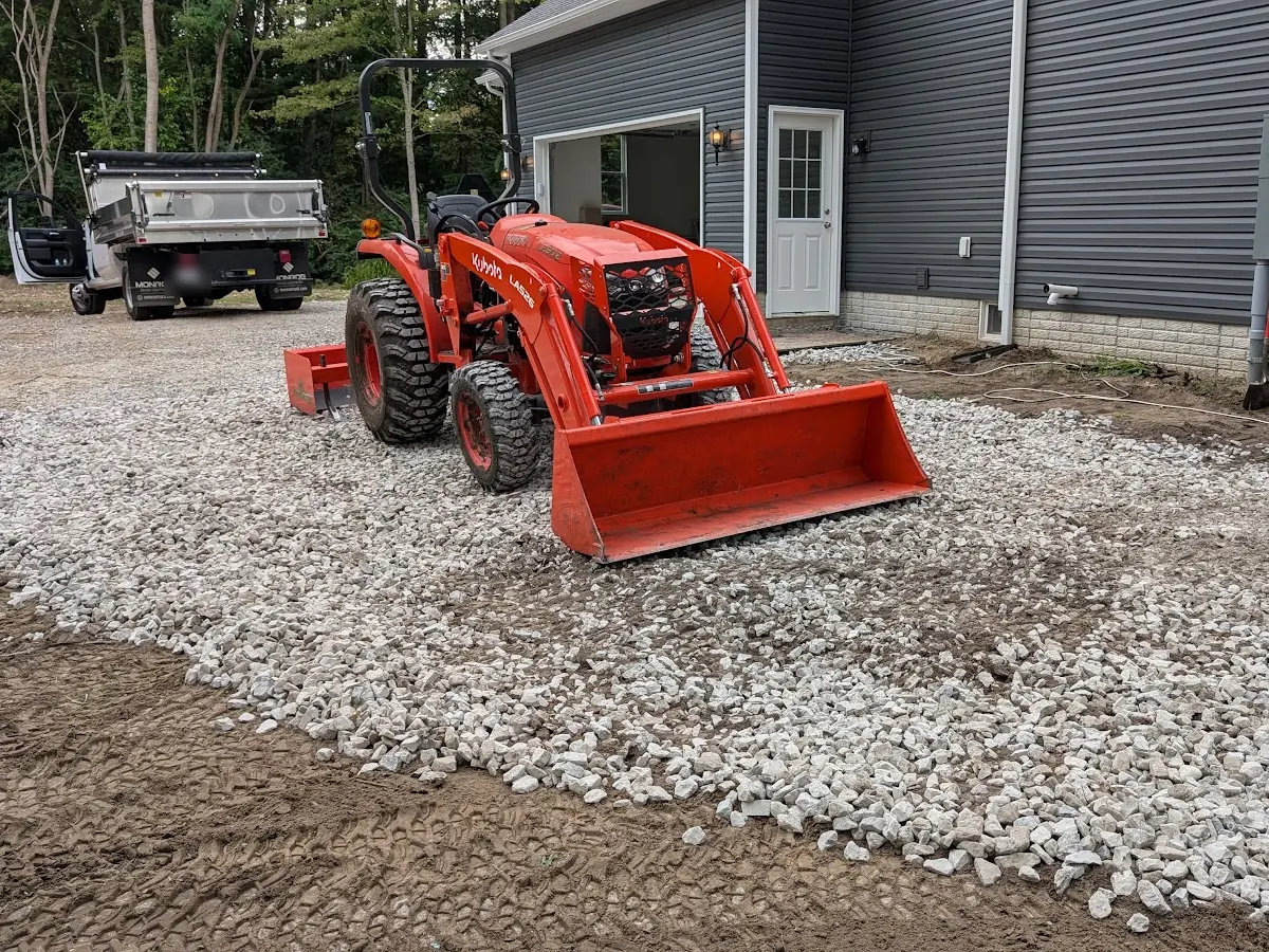 Orange tractor with a front loader on crushed stone beside a gray garage
