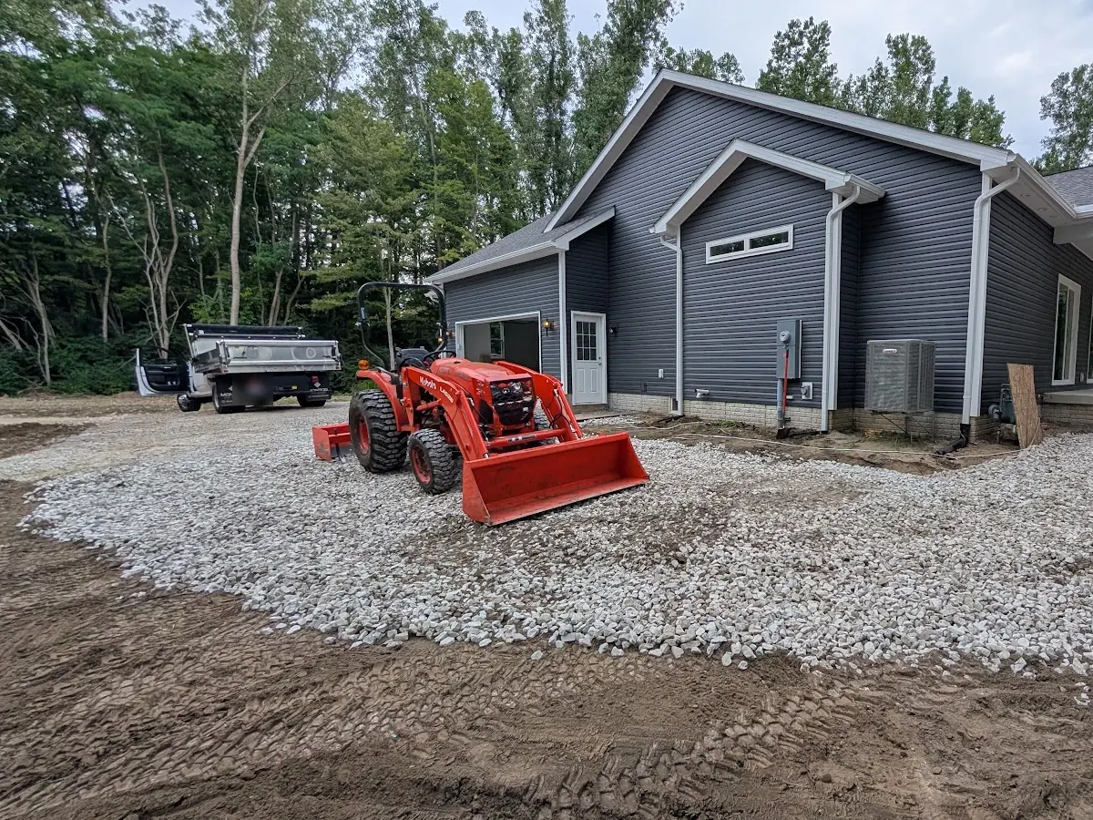 Orange tractor on a freshly spread crushed-stone area beside a gray house