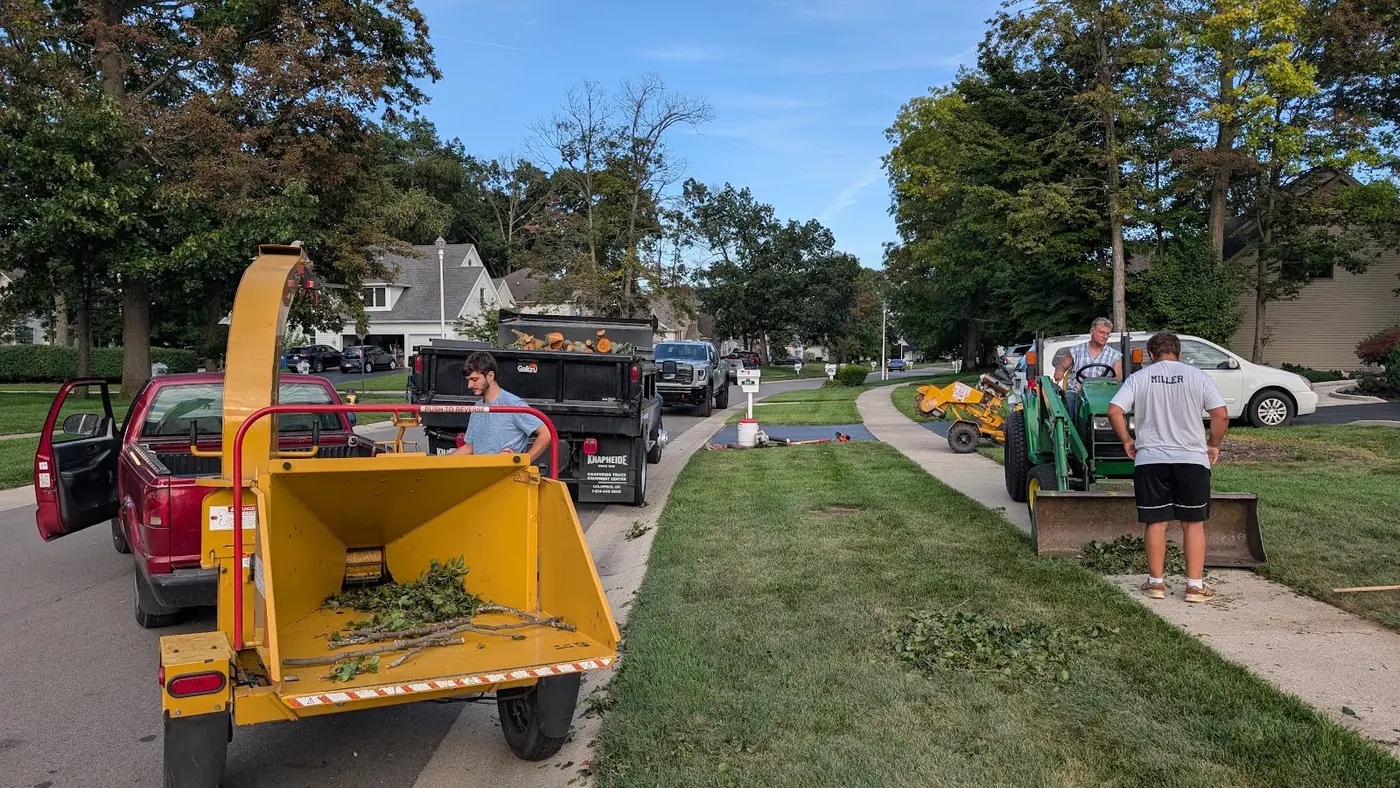 Wood chipper, dump truck and a small tractor with a crew on a residential street after tree work