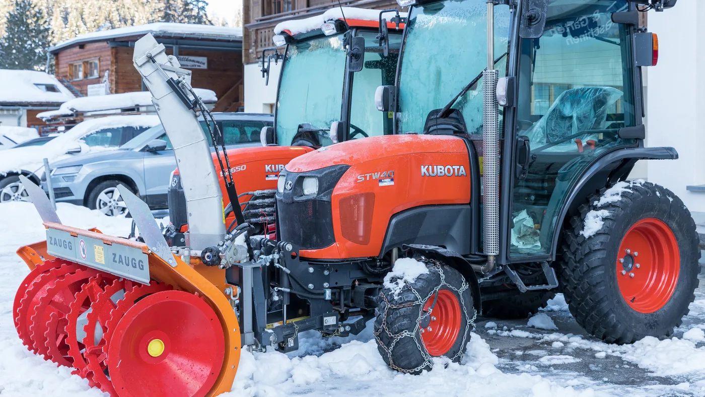 Orange Kubota compact tractor with a front-mounted snow blower, parked in the snow